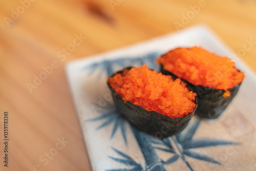 Close-up of two pieces of tobiko sushi (flying fish roe) on a ceramic plate.