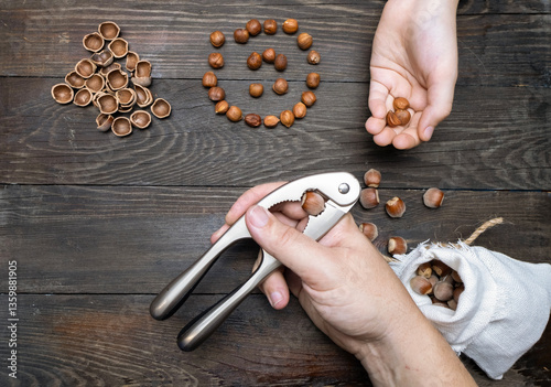 Cracking hazelnuts, male and child hands with nuts on wooden table.