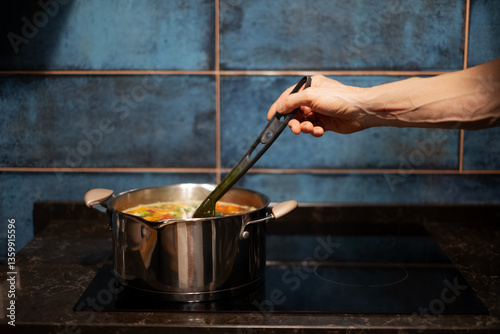 Tableau sur toile Man stirring soup on modern kitchen stove