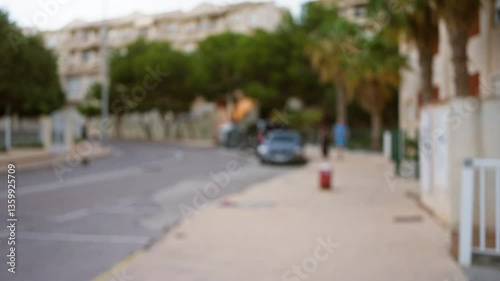 Wallpaper Mural Blurred outdoor scene of urban street with buildings and trees, sidewalk, and parked cars under defocused bokeh light, creating a dreamy atmosphere with an out of focus man walking Torontodigital.ca