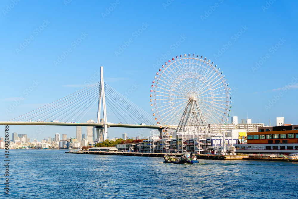 Naklejka premium Sunset view of Osaka city at Osaka bay area with Industries locate around, boat, Tempozan Farris Wheel and Tempozan bridge againt blue sky. Selective focus.