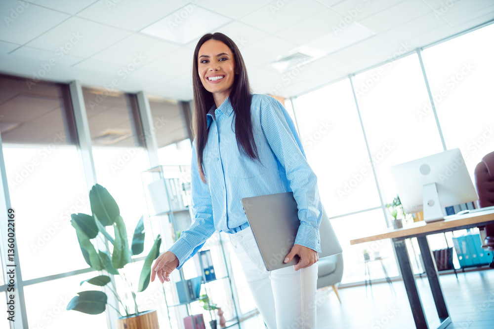 Professional businesswoman wearing formal attire smiling in a bright office workspace, holding a laptop and exuding confidence and success. Professional businesswoman wearing formal attire smiling in a bright office workspace, holding a laptop and exuding confidence and success.