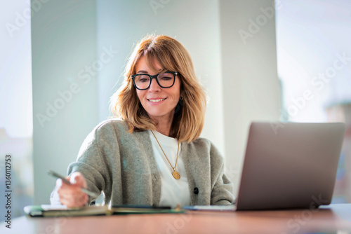 Blond haired businesswoman sitting in a modern office and using her laptop