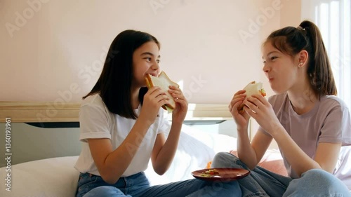 Two happy girls enjoying sandwiches together in a cozy bedroom