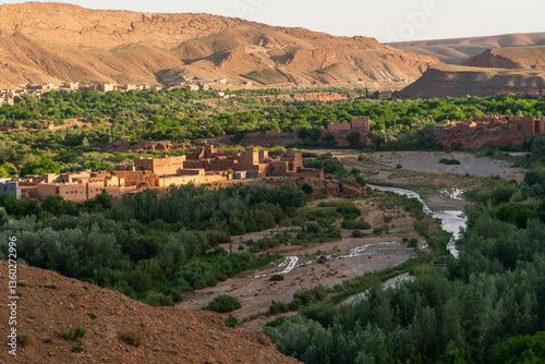 Ancient village in the middle of a green and leafy valley amidst red and desert mountains in Morocco