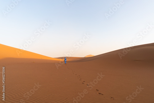 person walking on big sand dunes in the sahara desert in morocco on sunrise