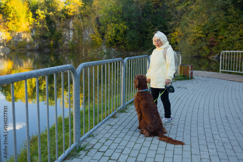 Obraz na płótnie Senior 60s woman crossbreed looking out over a lake with her best friend irish setter dog wear casual clothes in the autumn forest. w salonie