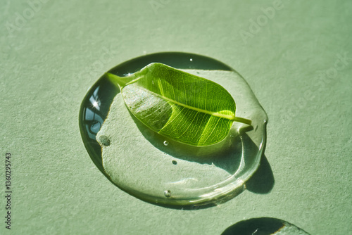 A drop of micellar water with a green leaf on a green background.