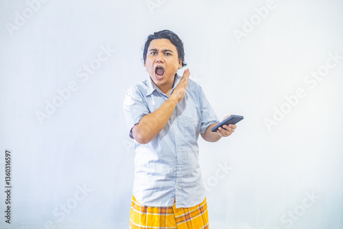 Portrait of surprised young Asian Muslim men showing blank screen on phone with copy space inside. Ramadan and Eid Mubarak concept