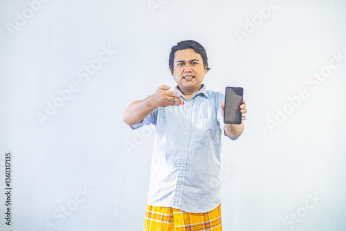 Obraz na płótnie Portrait of surprised young Asian Muslim men showing blank screen on phone with copy space inside. Ramadan and Eid Mubarak concept w salonie