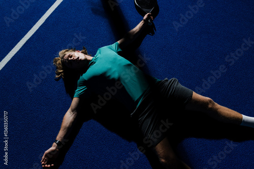 Exhausted player lying on padel court holding racket after intense match