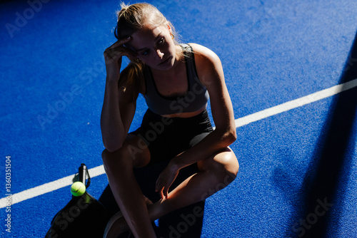 Woman resting on padel court, sitting with racket and ball nearby