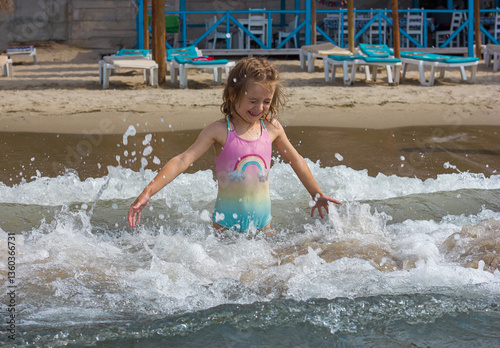 Beautiful happy little girl playing in the waves and splashes on the sea	