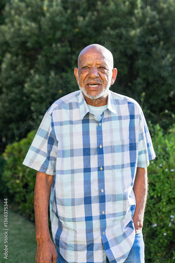 Senior man smiling outdoors in garden, enjoying sunny day in casual attire Senior man smiling outdoors in garden, enjoying sunny day in casual attire
