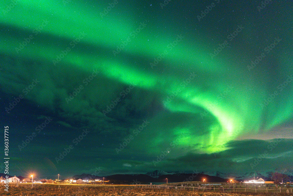 Fototapeta premium Beautiful Aurora Borealis over house on the island of Kvaløya, dancing northern lights with green light, red and purple strikes, clear colored rays of light in the sky, amazing joy in Norway