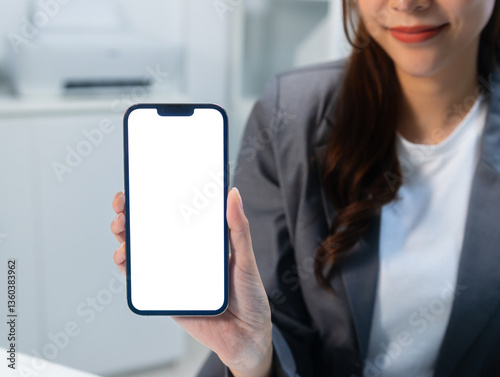 Close up of business woman hand holding smart phone with white blank screen mockup with modern office space background. mobile phone mockup with empty space and blank screen for advertise.