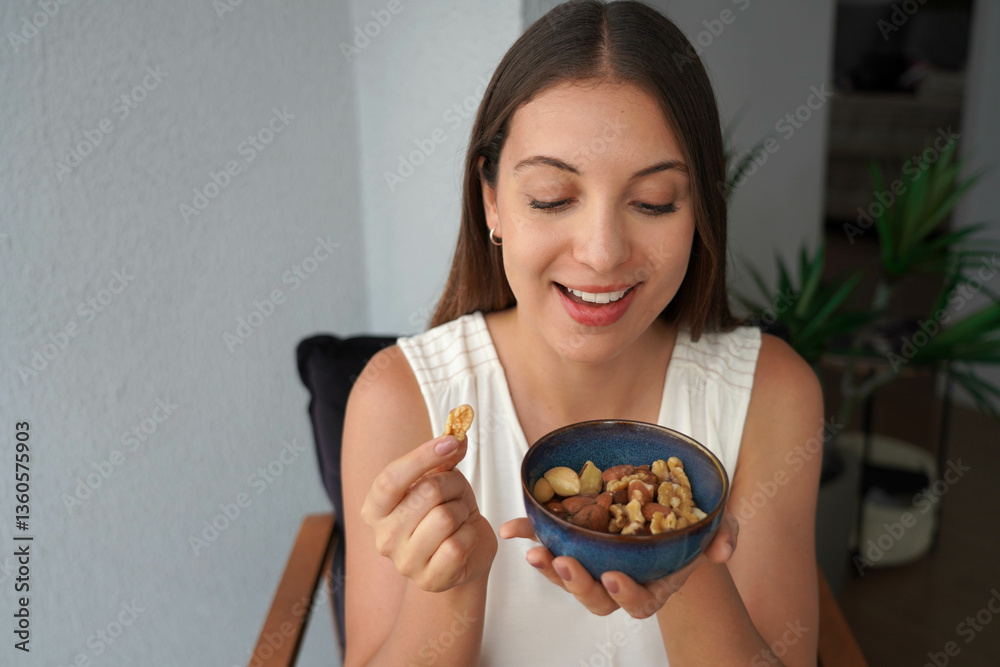 Pretty healthy girl picking mix of nuts dried fruits from bowl as snack at home