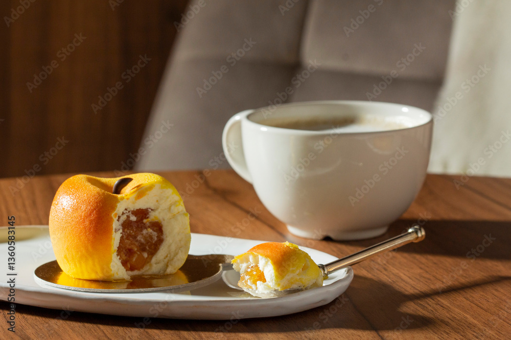 Mousse cake with peach filling covered with velvet glaze and a cup of latte on a table in a cafe.