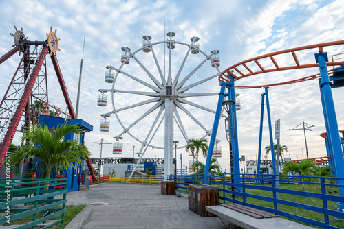 Ferris wheel and roller coasters at a closed and empty amusement park, sunny day, blue sky with white clouds. Sunset Park in La Libertad tourist beach town, El Salvador.	