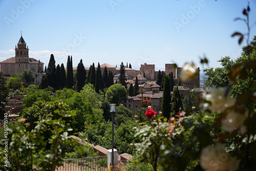 Historic Alhambra Palace surrounded by lush green trees and red flower on a sunny day, Granada, Spain - Beautiful Moorish Architecture and Gardens (188 characters)
