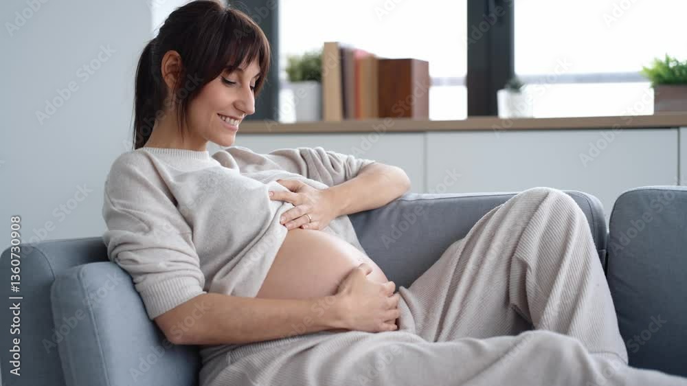 Video of beautiful pregnant woman relaxing while touching her belly sitting on couch at home Video of beautiful pregnant woman relaxing while touching her belly sitting on couch at home