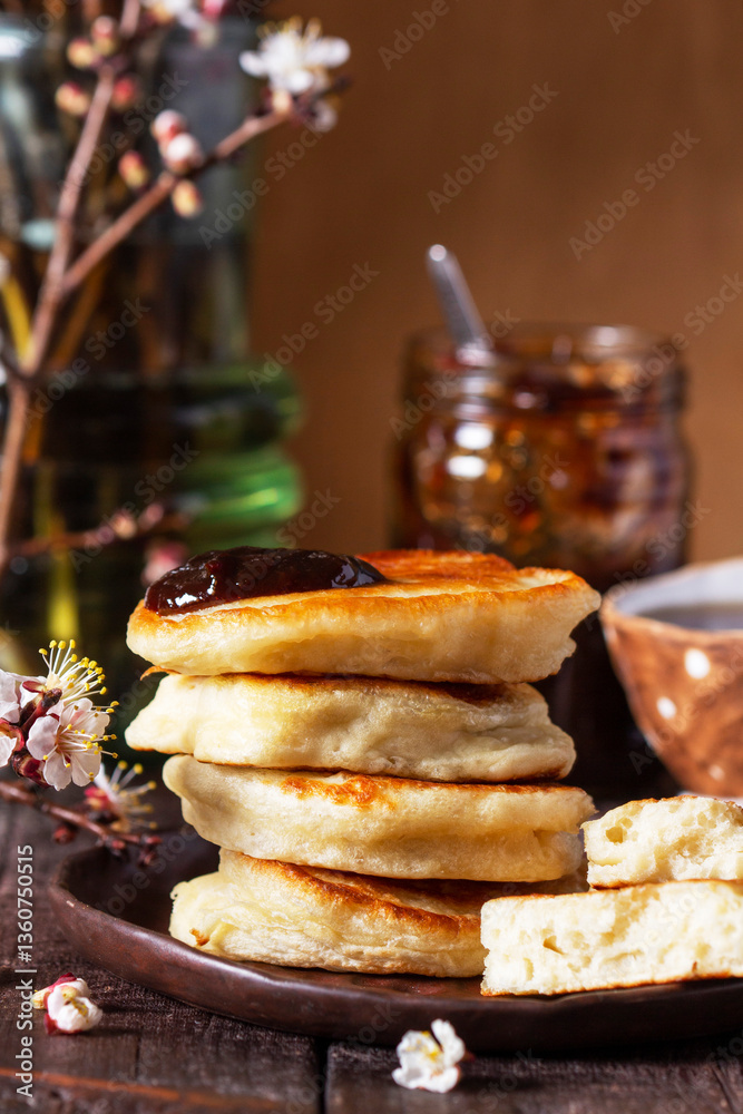 Lenten yeast pancakes with plum jam and tea, and a bouquet of blooming apricot branches on a wooden table.