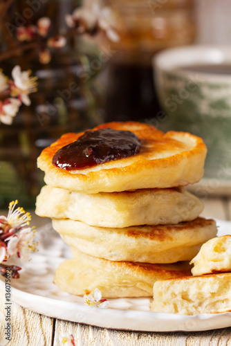 Lenten yeast pancakes with plum jam and tea, and a bouquet of flowering apricot branches on a light wooden table.
