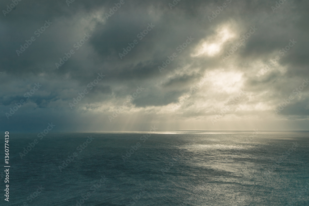 Fototapeta premium Lighthouse on the rockHeavy storm clouds over the sea with rays of sunshine