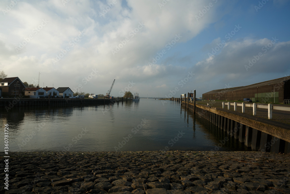 Obraz premium Calm waters reflect the cloudy sky along the quiet harbor in the late afternoon