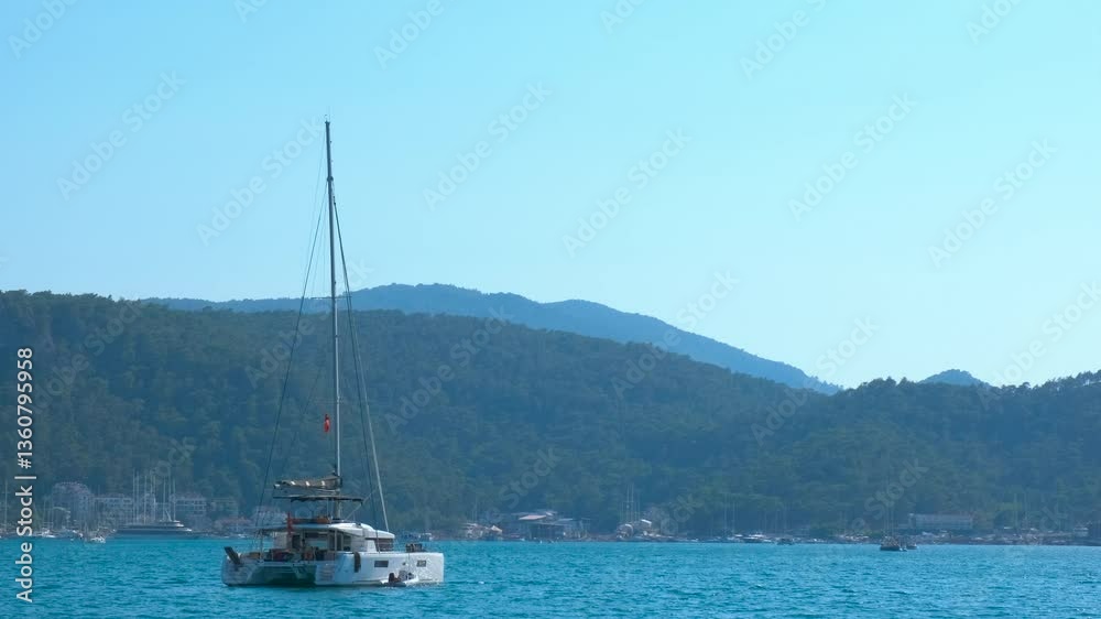 Warm sea waves with sailing one yacht. A view of warm sea waves with sailing small cruise catamaran against blue hills during summer weekend. Warm sea waves with sailing one yacht. A view of warm sea waves with sailing small cruise catamaran against blue hills during summer weekend.