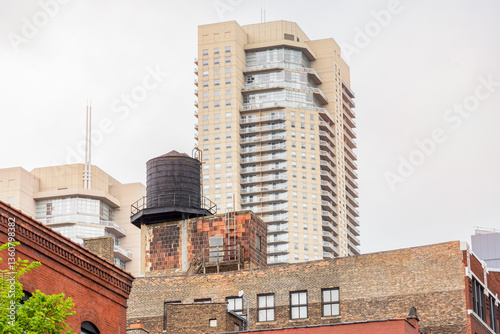 Traditional black water tank on the roof of an old brick building in downtown Chicago. A modern apartment tower is in background.