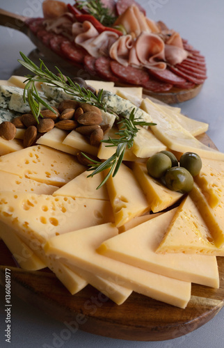 Finger food. Closeup view of a cheese board, with gruyere, blue cheese, feta, and a cold cuts plate, with salami, ham and prosciutto, in the background