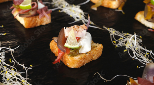 Gourmet finger food. Canapes. Closeup view of a mediterranean bruschetta with different ingredients such as cheese, ham and vegetables, presented in a black board