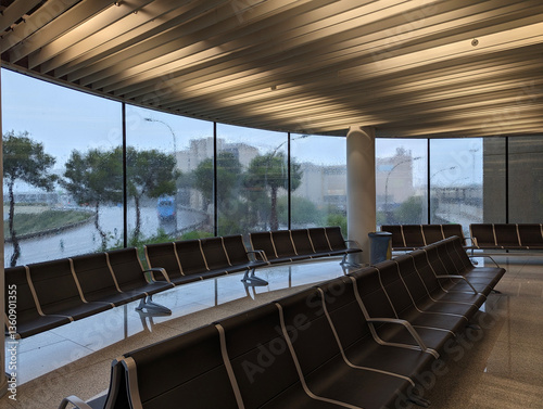 Modern waiting area interior at international airport with empty seats  large wet windows on rainy spring day. Heavy rainfall  rainwater droplets  stormy weather  delay and travel waiting atmosphere. 