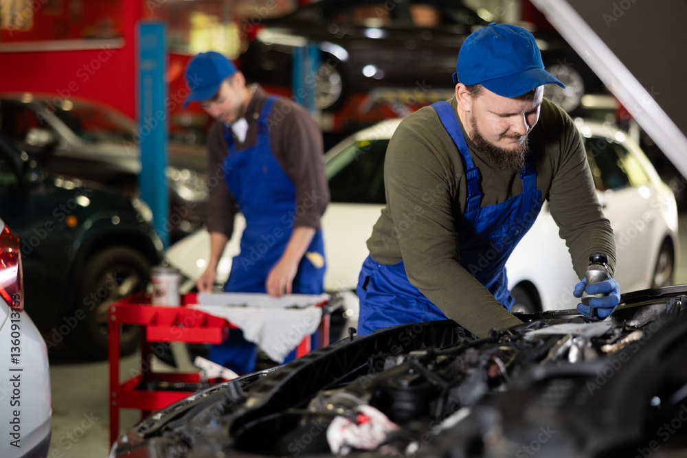 Fototapeta premium Proficient car mechanic in blue uniform checking auto-details in auto repair shop
