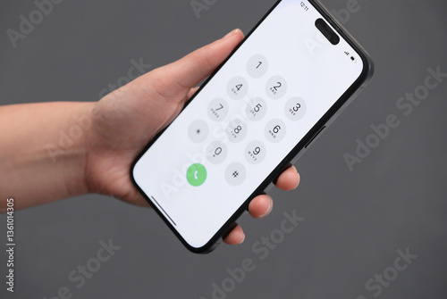 Woman holding smartphone with dialer application against blurred grey background, closeup
