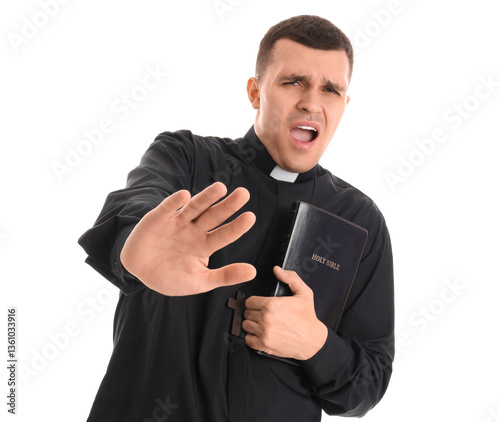 Scared young priest with Holy Bible on white background