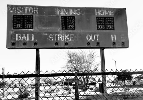 faded retro baseball scoreboard with chipped paint rusty metal vintage numbers cracked surface surrounded by weeds old lights above evoke nostalgia from decades of summer games and crowds cheering
