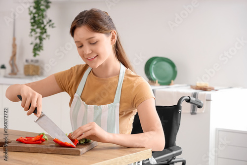 Young woman in wheelchair cutting bell pepper at home photo
