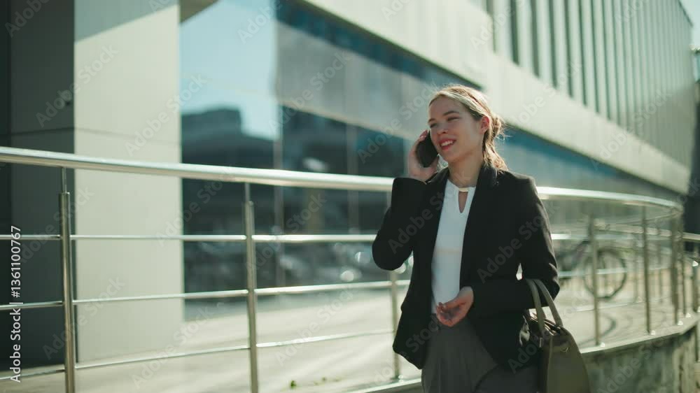 Professional business lady walking home smiling during phone call, dressed in formal attire, holding handbag, enjoying conversation under bright sunlight, urban glass building Professional business lady walking home smiling during phone call, dressed in formal attire, holding handbag, enjoying conversation under bright sunlight, urban glass building