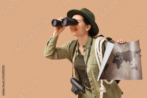 Slika na platnu Young female tourist with map looking through binoculars on beige background
