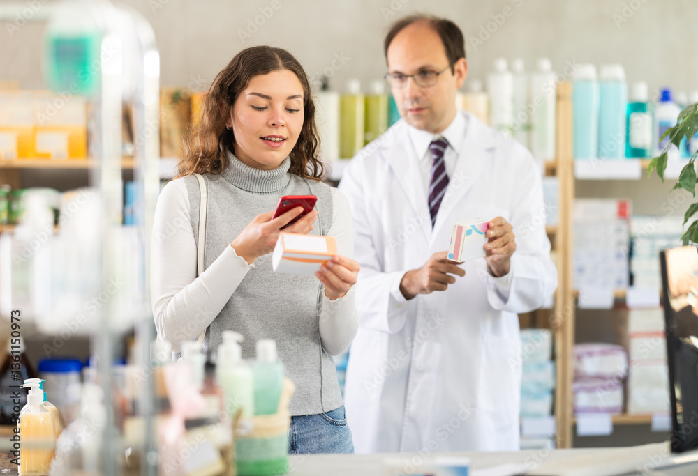 Fototapeta premium Young woman buyer scanning qr code for box of pills with adult man pharmacist in pharmacy