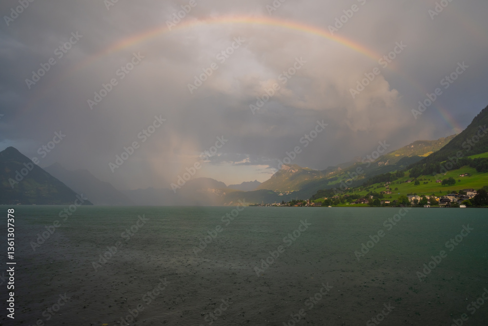 Fototapeta premium Rainbow background. Swiss Alps mountain on rainy day with rainbow. Mountain under rainbow. Rainbow nature background. Blue lake near mountain.