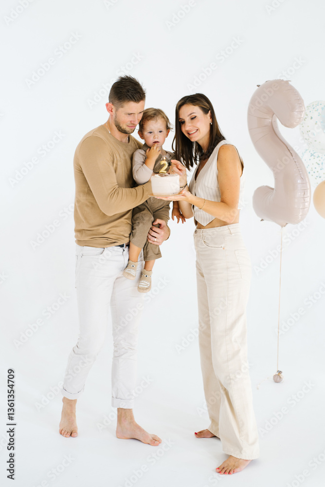 Young couple and their child are posing for a picture in front of a birthday cake
