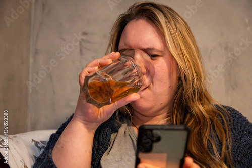 Caucasian mother enjoying a drink while interacting with her smartphone at home