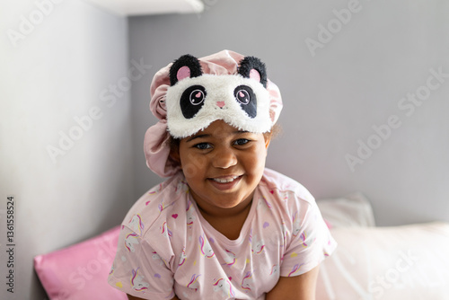 Smiling mixed race girl waking up in pink sleepwear and hair bonnet