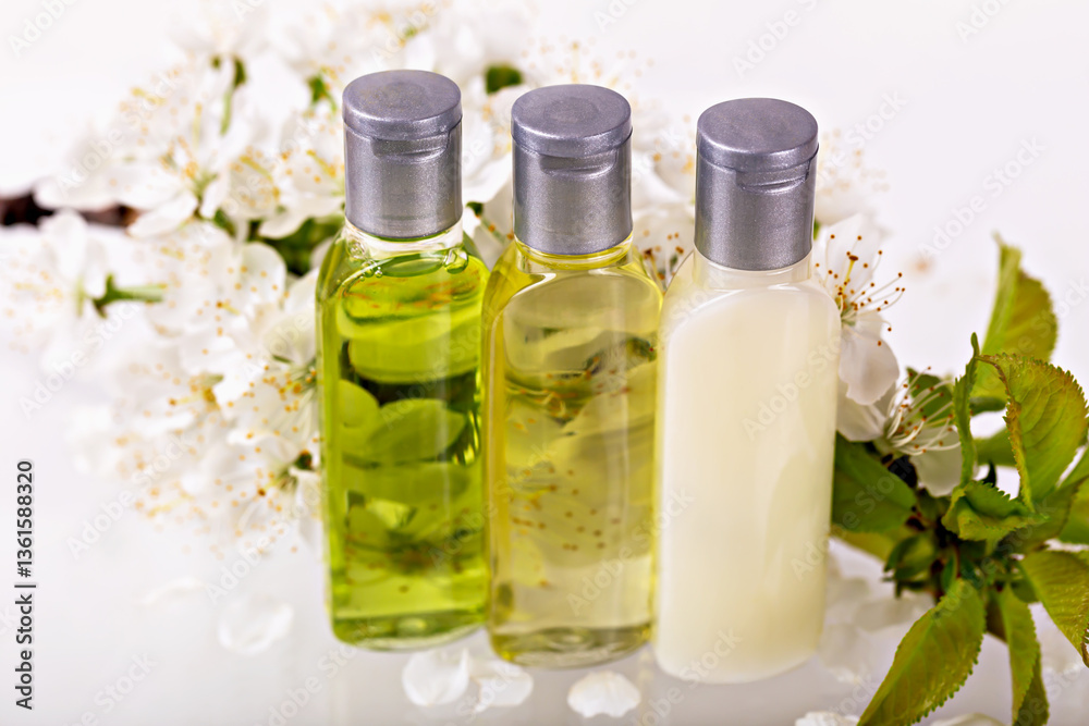 Three transparent bottles with silver caps containing skincare oils and lotion are placed among fresh white blossoms. Natural aesthetic emphasizes organic beauty, wellness and self-care concepts Three transparent bottles with silver caps containing skincare oils and lotion are placed among fresh white blossoms. Natural aesthetic emphasizes organic beauty, wellness and self-care concepts