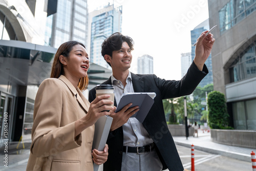 Asian young businessman and woman partner working outdoors in city. 