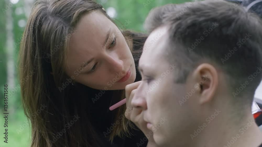 Professional makeup artist carefully applying Halloween makeup on a man's face, transforming his appearance for a spooky celebration in a forest Professional makeup artist carefully applying Halloween makeup on a man's face, transforming his appearance for a spooky celebration in a forest