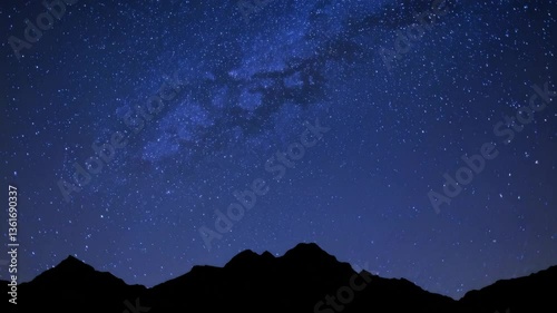 Timelapse of starry night sky over silhouetted mountains with milky way unveiling